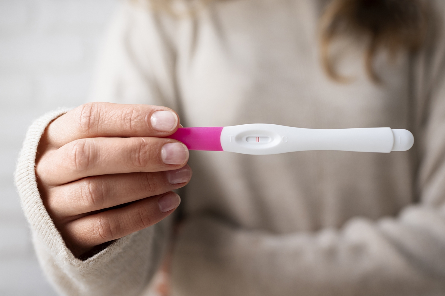 Woman holding a positive pregnancy test showing two lines, symbolising early pregnancy and the first weeks of foetal development.